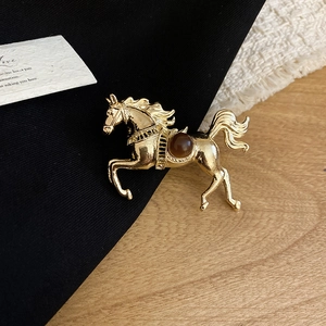 Detailed view of a gold horse brooch featuring a brown resin stone on a textured backdrop