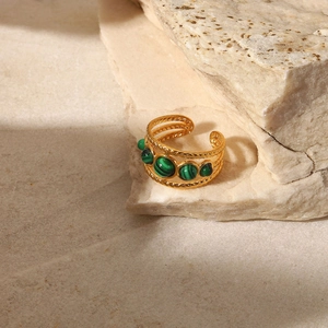 Detail of gold braided ring with green malachite stones on natural beige stone