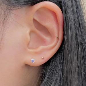 Detail of 925 silver iridescent crystal stud and golden bead earrings on model ear