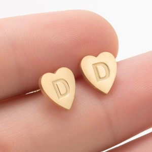 Vue macro de boucles d'oreilles cœur dorées avec lettre D et texture métal brossé
