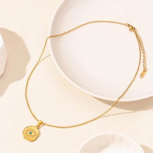 Detail showing the S.STEEL material stamp and evil eye pendant on a gold necklace