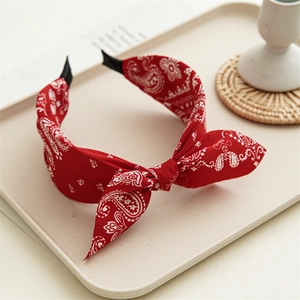 Detail of red paisley knotted headband with bow accent on a minimalist beige tray