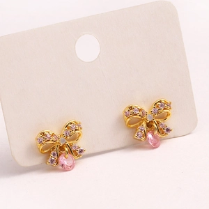 Detail view of gold bow earrings featuring pink zircon and a teardrop-shaped gemstone drop