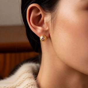 Detail of vintage 18k gold plated round earring with purple gemstone on model