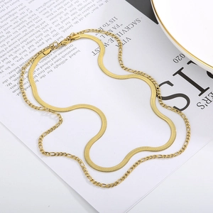 Flat lay of double-layered gold snake and Figaro chain necklaces on book pages