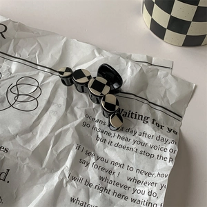 Close-up of black and white checkerboard hair clip on a vintage newspaper background
