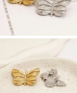 Close-up of butterfly brooch with hammered texture and sparkling crystals on a ceramic tray