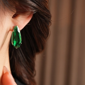 Close-up of deep green pear-cut zircon earrings set in silver metal on a model's ear