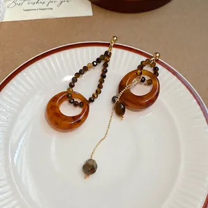 Boucles d'oreilles asymétriques en résine œil de tigre et chaîne dorée sur plat blanc