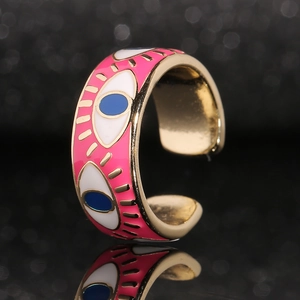 Macro shot of gold adjustable ring with pink enamel and evil eye charms over black backdrop