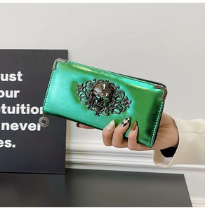 Close-up of metallic green wallet with skull and floral badge and zip closure