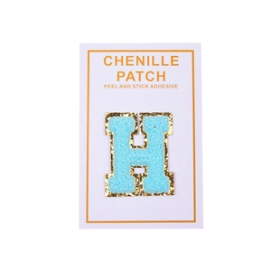 Close-up of light blue chenille letter H patch with gold glitter border and adhesive back