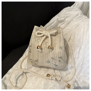 Close-up of woven straw bucket bag featuring delicate floral embroidery and drawstring