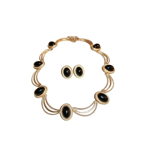 Vintage gold necklace and earring set with black oval gemstones on white backdrop
