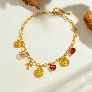 Gold vintage necklace with saint coin, cross, and heart charms on a beige surface