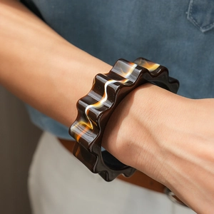 Primo piano del bracciale rigido in acrilico ambrato con bordi ondulati e texture