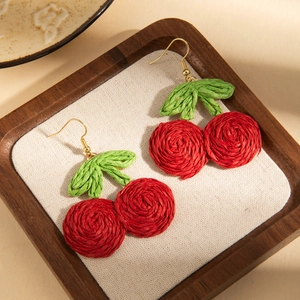 Close-up of handmade woven cherry earrings with red fruit and green leaves on wood
