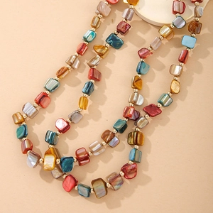 Macro view of multi-color shell bead necklace with golden spacers on a beige surface
