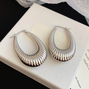 Detailed view of silver ribbed U-shaped hoop earrings on minimalist white packaging