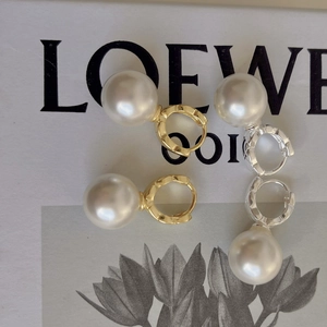 Detail view of large pearl drop earrings in gold and silver finishes with sleek hoop clasps