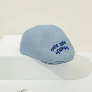 Detail of light blue denim baby beret featuring dark blue COME HERE OFFROAD embroidery