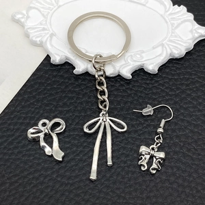 Silver bow alloy charms displayed with keychain and earring on black textured surface