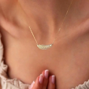 Macro view of golden feather pendant with fine textures on a delicate chain necklace