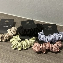 Detail view of five assorted satin silk scrunchies in champagne, black, green, blue, and pink