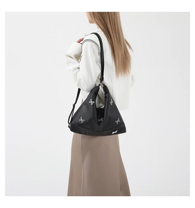 Detail of black triangular shoulder bag featuring metallic butterfly accents on nylon fabric