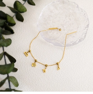 Detailed view of 18K gold-plated zodiac charms on a dainty stainless steel chain bracelet