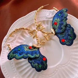 Vintage gold hoop earrings with butterfly embroidery and rhinestones on ceramic plate