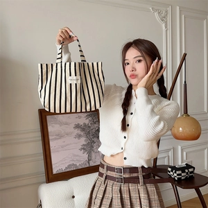 Detail of a large black and white striped canvas tote bag held by a model in a cozy room