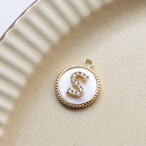 Macro detail of gold plated letter S pendant with white shell and inlaid zircons