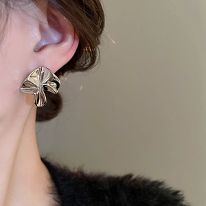 Close-up of irregular pleated flower stud earring with silver metallic finish on ear