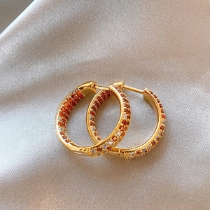 Macro detail of gold huggie earrings with orange and white zircon on silk fabric