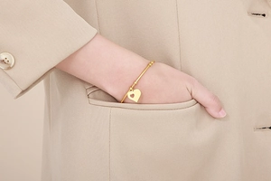 Detail of elegant gold heart pendant bangle worn on a wrist with neutral suit sleeve