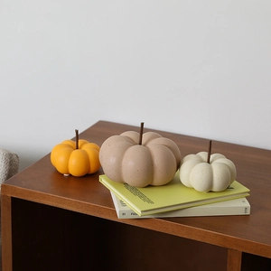 Three assorted ceramic pumpkin ornaments in orange, beige, and tan on a wooden table