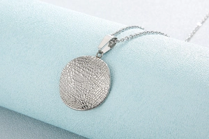 Macro detail of a silver round pendant featuring an abstract textured pattern on an O-chain