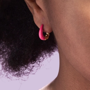 Pink enamel U-shaped croissant hoop earrings worn by a model in a fashion close-up view
