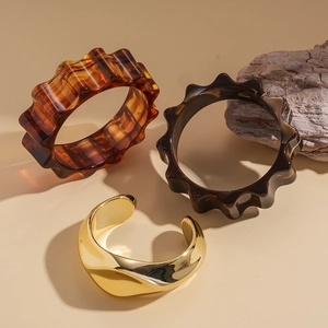 Three-piece acrylic tortoiseshell and gold metal bangle set on a wooden base