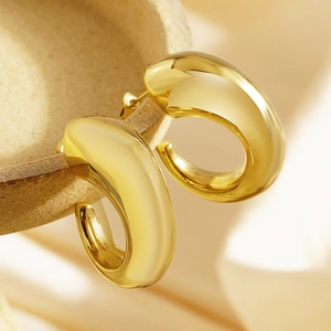 Macro view of gold chunky C-shaped hoop earrings with polished mirror finish on ceramics