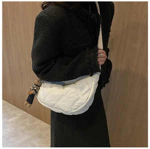 Detailed view of a white quilted crossbody bag with a cute bear charm on a female model