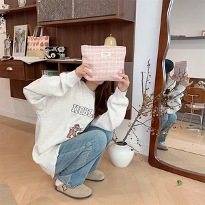 Close-up of a pink tweed textured toiletry bag held by a model in a cozy home setting