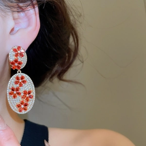 Close-up of vintage gold drop earrings with red flower patterns and pave zircons