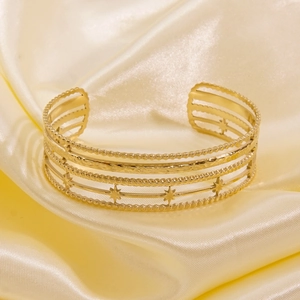 Detail view of gold titanium steel open bangle with layered stars on satin background