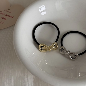 Close-up of gold and silver alloy bow hair ties on elastic bands in a ceramic bowl