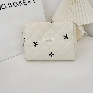 Close-up of quilted cream makeup bag with black bow embroidery and Sezakka woven label