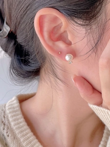 Close-up of model wearing round white pearl earrings with gold base and zircon detail