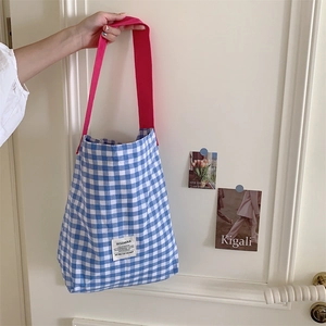 Détail d'un cabas en toile à carreaux bleus avec bandoulière rose suspendu à une porte