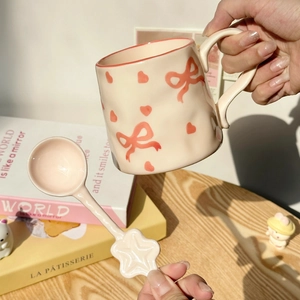 Cute beige ceramic mug with pink bow patterns and a matching star-tipped spoon